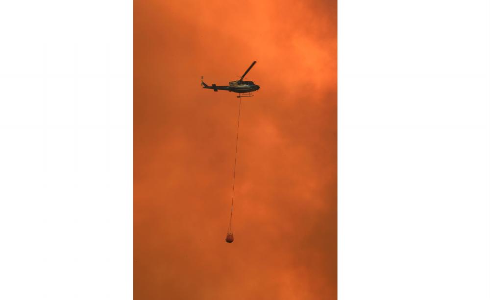 A helicopter drops water on a homestead as bushfires impact on farmland near the small town of Nana Glen, some 600km north of Sydney on Nov 12. — AFP