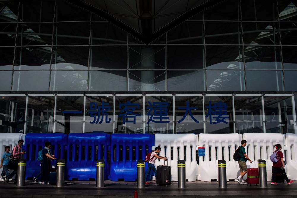 Passengers walk past water filled barricades put in place by police as they walk towards a new security check point at the entrance of Chek Lap Kok, Hong Kong's international airport, on August 24, 2019. - AFP