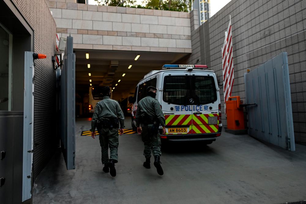 Police officers walk next to a police vehicle after a bus believed to be carrying detained protesters arrived at the West Kowloon Law Courts building in Hong Kong on November 20, 2019. - AFP