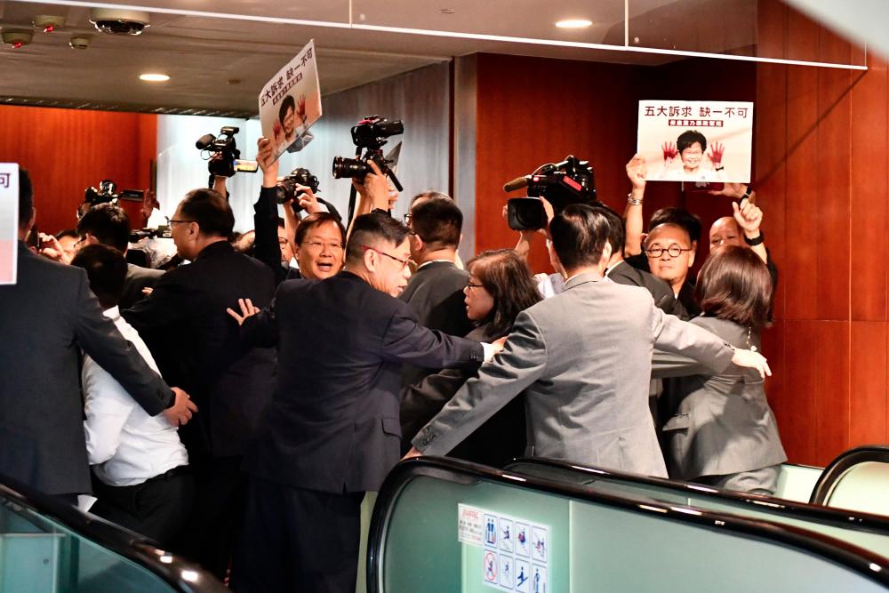 Security tries to control members of the press and protesting pro-democracy lawmakers after Hong Kong's Chief Executive Carrie Lam (pictured on placards) had to leave the chamber for a second time while trying to give her annual policy address at the Legislative Council (Legco) in Hong Kong on Oct 16, 2019. — AFP