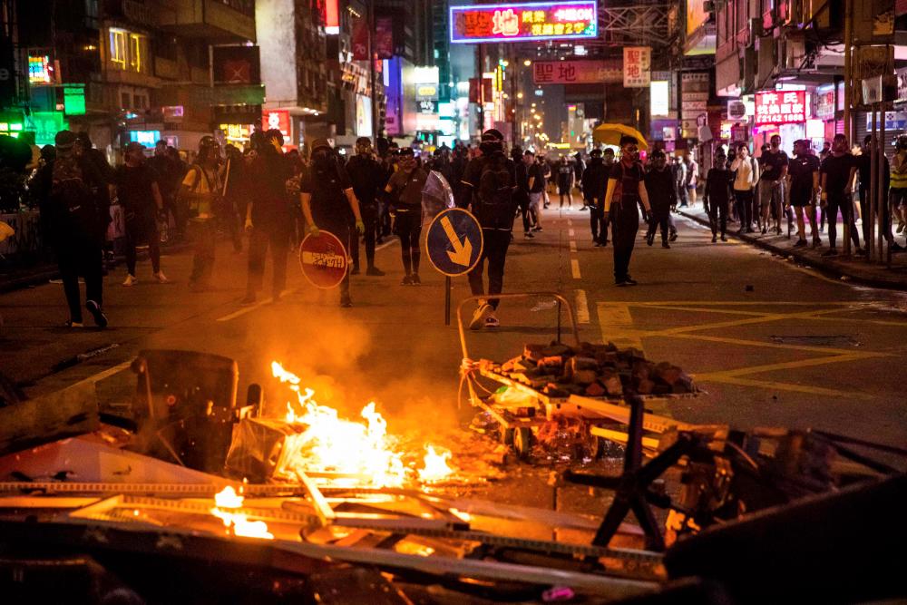 Protesters retreat from a burning barricade as police advance in the Mong Kok district in Hong Kong on Oct 20, 2019. — AFP