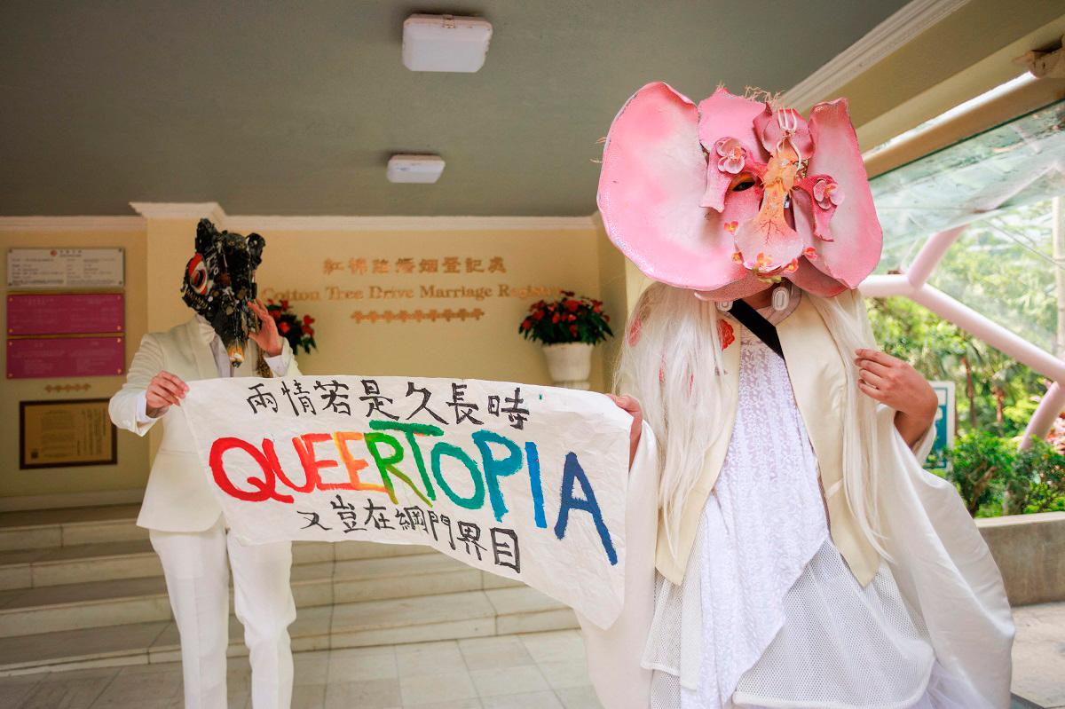 This photo taken on July 28, 2025 shows non-binary performance artist Holok Chen (R) and a model who requested anonymity holding a banner that reads “If the love is meant to endure, why should it be confined to portals and digital boundaries” as they promote LGBTQ equality outside the Cotton Tree Drive Marriage Registry in Hong Kong. Hong Kong’s LGBTQ community has reluctantly rallied behind a government plan that could expand rights for same-sex couples, with “desperate” activists ditching their idealism in hopes of a rare legislative win. - May JAMES / AFP