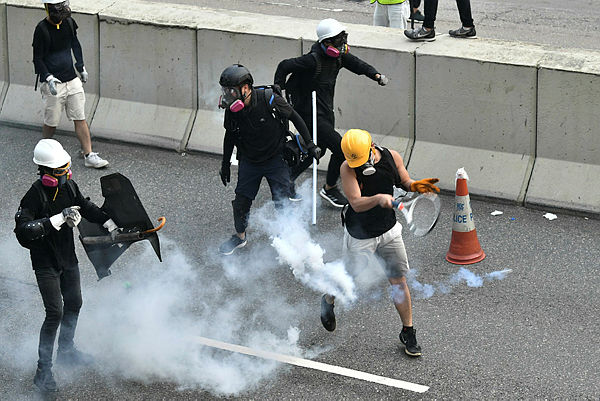 A protester (R, in yellow helmet) swings a tennis racquet to return a tear gas canister fired by riot police at Kowloon Bay in Hong Kong on Aug 24.