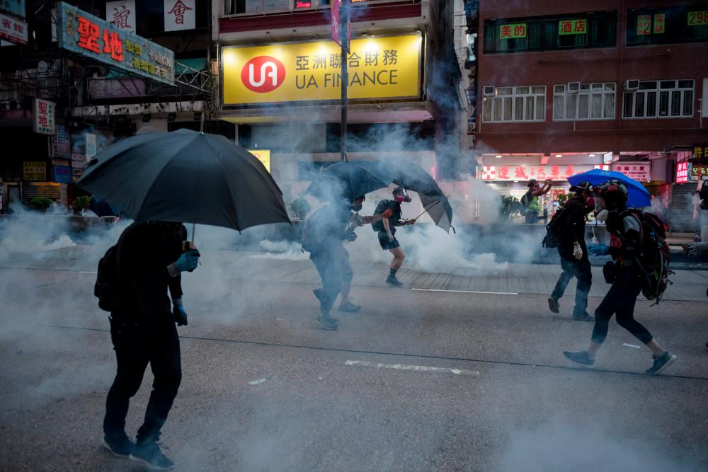 Protesters react to tear gas fired by police during a pro-democracy march along Nathan Road in the Kowloon district in Hong Kong on Oct 20, 2019. — AFP