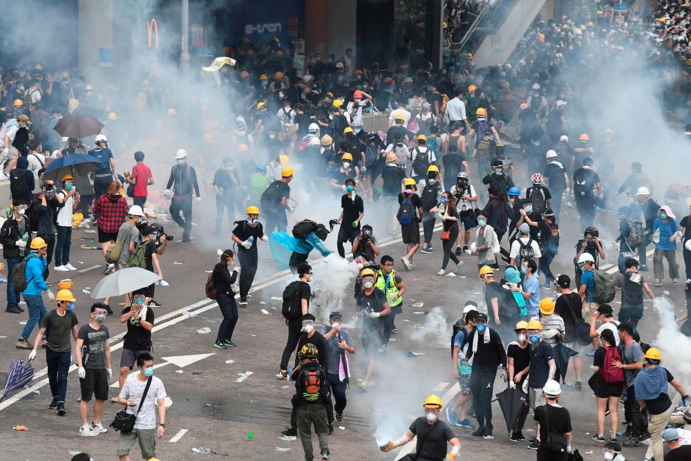 Protesters react after police fired tear gas during a rally against a controversial extradition law proposal outside the government headquarters in Hong Kong on June 12, 2019. Violent clashes broke out in Hong Kong on June 12 as police tried to stop protesters storming the city's parliament, while tens of thousands of people blocked key arteries in a show of strength against government plans to allow extraditions to China. — AFP