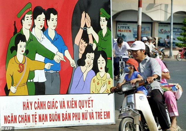 A Vietnam family rides past a poster appealing to people to be vigilant against human trafficking in Ho Chi Minh City. — AFP
