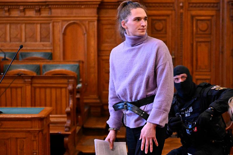 The defendant, German anti-fascist activist Maja T, stands while being held on a leash by a police officer during a preliminary court hearing in Budapest on February 21, 2025 for allegedly participating in attacks against presumed neo-Nazis on the streets of the Hungarian capital. The case sparked uproar in Germany, with the country's top court saying the extradition order for the suspect, who identifies as non-binary, had failed to take into account potentially dangerous prison conditions in Hungary, especially for LGBTQ people. The defendant is accused of four counts of attempted assault as part of a criminal organisation aiming to send a deterrent message to members of extreme-right movements by inflicting various life-threatening injuries according to a court statement. - Attila KISBENEDEK / AFP