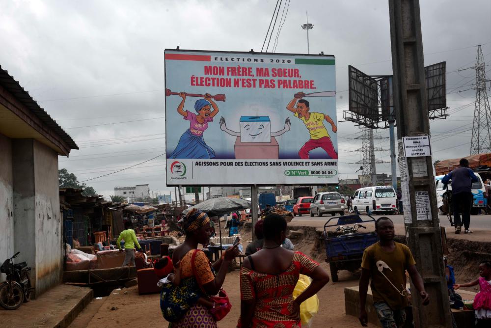 People walk past a billboard in Yopougon, a popular district of Abidjan, on Sept 16, 2020, promoting peaceful elections in Ivory Coast set for the month of October. — AFP