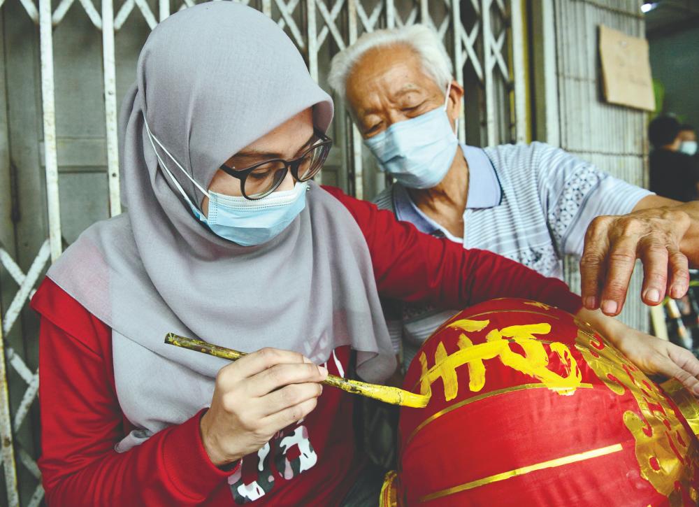 Cheng keeping a close watch as Azizah puts the final stroke to a Chinese character on a lantern at his shop in Kulai, Johor. – BERNAMAPIX