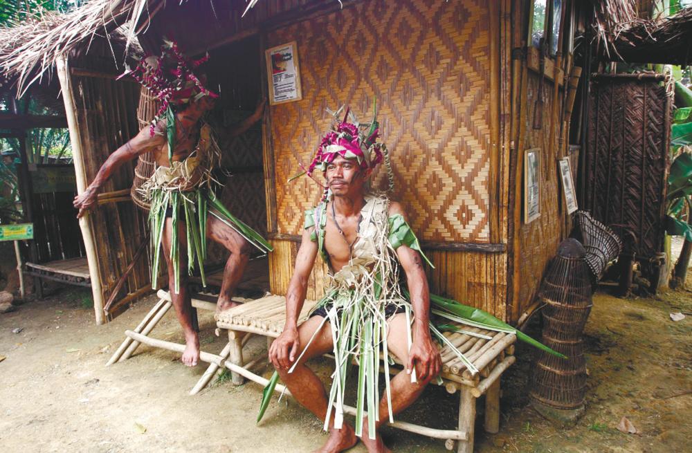 $!Orang Asli in traditional attire pose for photographs in front of a traditional house during the Orang Asli Art and Culture Carnival at Padang Perkampungan Orang Asli Rasau Hilir, Batu 14 Puchong. – Asyraf Rasid/thesun