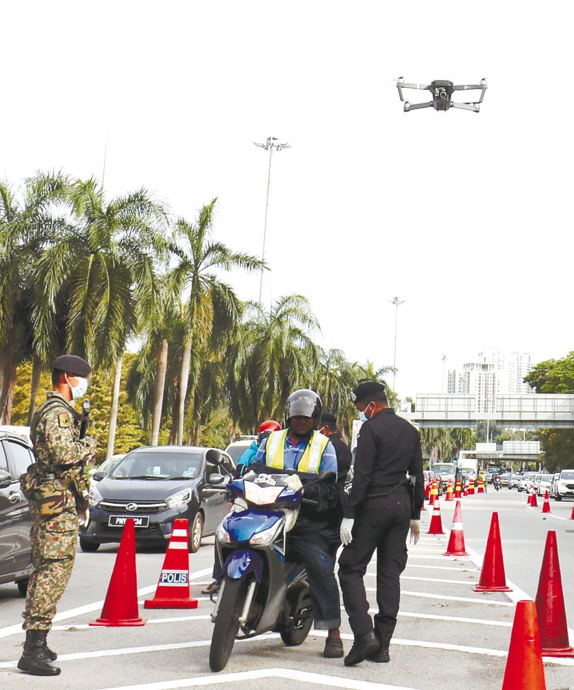 $!Eye in the sky ... A drone used to monitor people’s movement hovers above as a police officer stops a motorcyclist to check his documents at a roadblock on Tun Dr Lim Chong Eu Expressway in George Town yesterday. – MASRY CHE ANI/THESUN