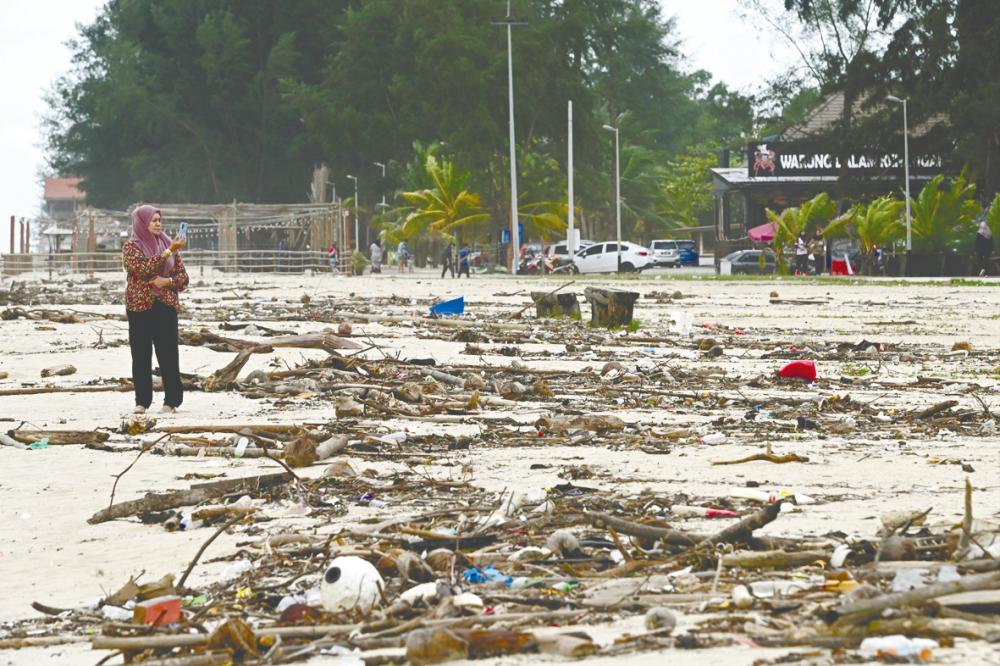 HIGH TIDE WOES ... Branches, twigs and garbage strewn along the sand, washed up by waves during the northeast monsoon season at the Batu Burok Beach in Terengganu yesterday. – BERNAMAPIC