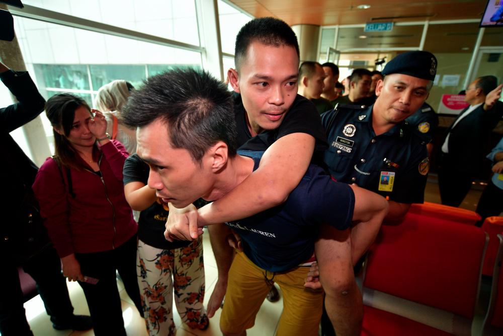 Mark Roger, 24, is carried by a friend on arrival at the Kuching International Airport on Feb 17, 2019. Roger, who has leg injuries, is among the 47 Malaysians who have returned after being detained in Poipet, Cambodia since Dec 11, 2018. — Bernama
