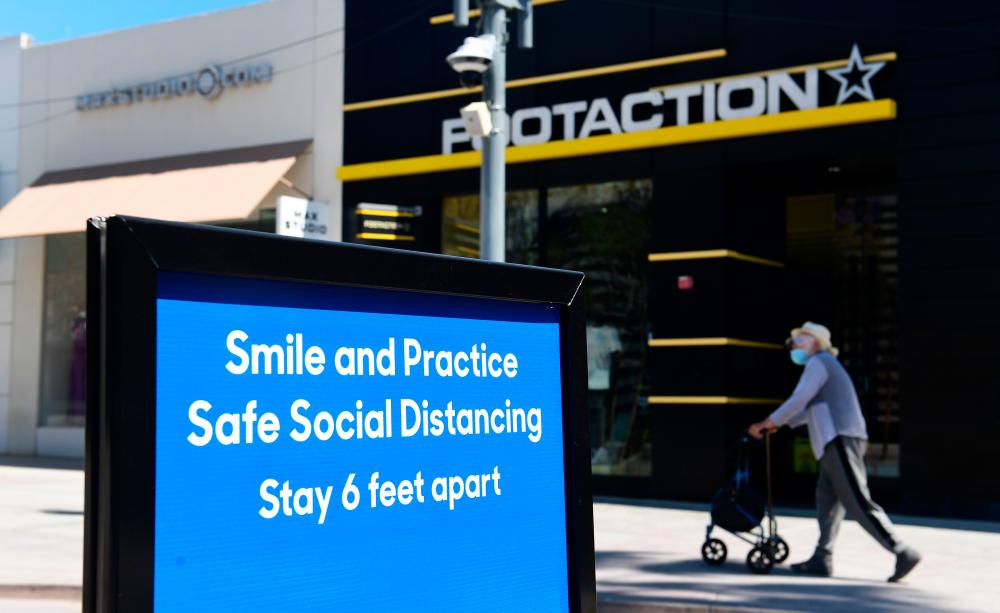 A sign along the Third Street Promenade shopping street in Santa Monica, California, reminds the public of social distancing rules. The IMF says the US economy will shrink 8% this year. – AFPPIX