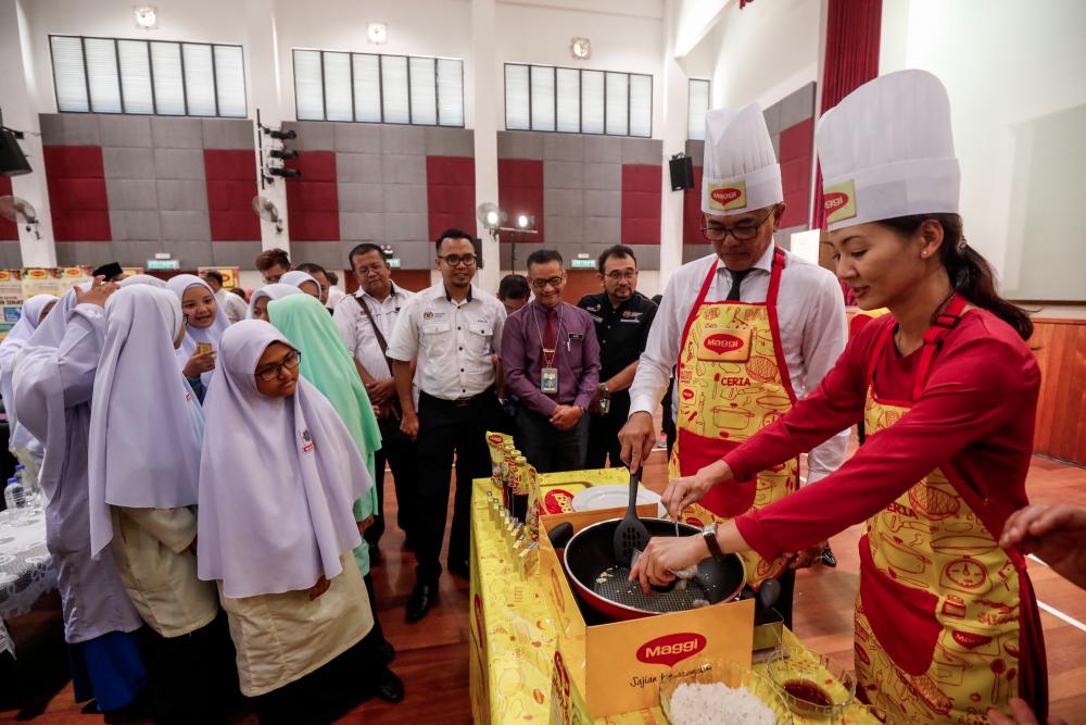 Students and officials look on as Education Ministry sports education and culture division deputy director Suhaimi Sun Abdullah (R2) and Maggi marketing manager Kimberly Oh (L) cook at the officiation of the 23rd Maggi Secondary Schools Cooking Competition 2019 at Sekolah Menengah Kebangsaan Agama Presint 11, Putrajaya on March 19, 2019. — Sunpix by Ashraf Shamsul