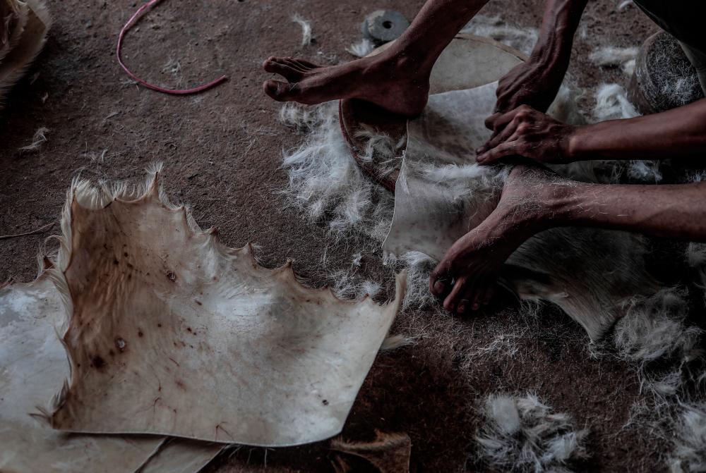 $!Workers scrape away hair from dried goat skin using a blade.