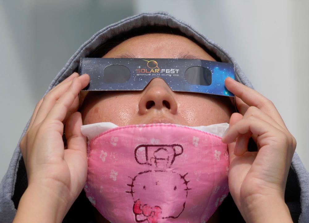 A women, wearing a protective face mask against the coronavirus disease (COVID-19), uses special protective glasses to watch a partial solar eclipse at Planetarium Negara . ASYRAF RASID/THESUN