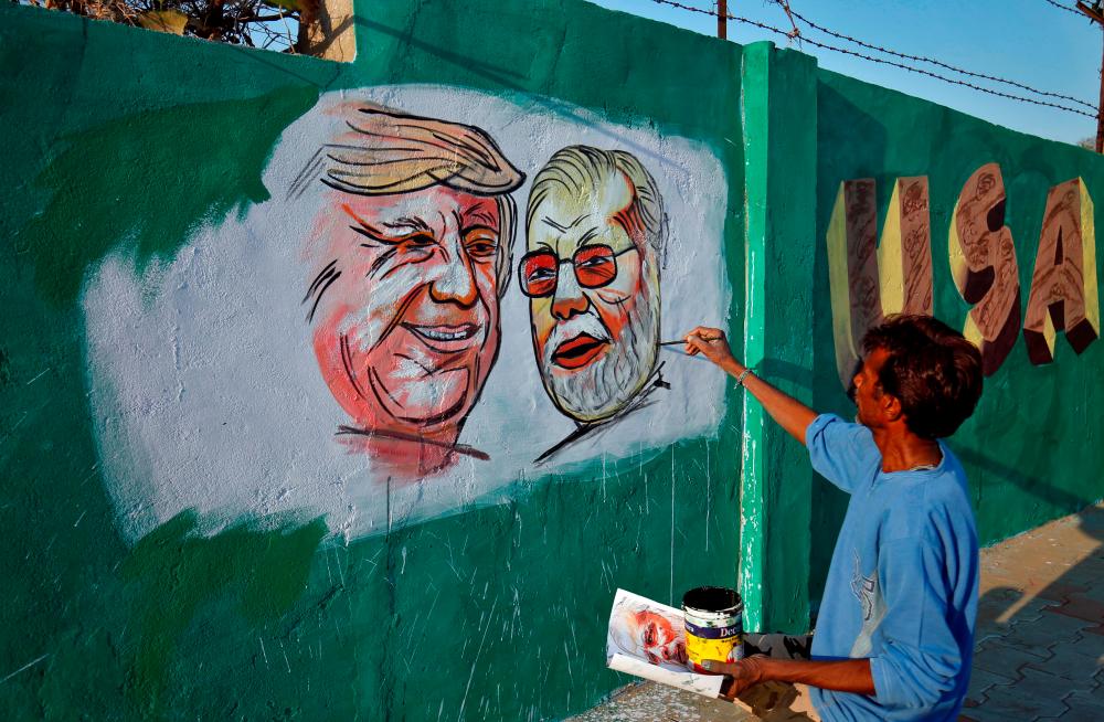A man applies finishing touches to paintings of US President Donald Trump and India's Prime Minister Narendra Modi on a wall as part of a beautification, along a route that Trump and Modi will be taking during Trump's upcoming visit, in Ahmedabad, India, February 17, 2020. - Reuters
