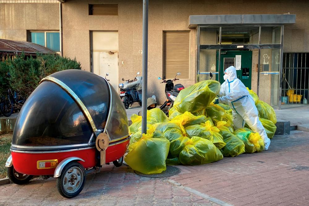 A pandemic prevention worker in a protective suit piles up bags of medical waste outside a building where residents isolate at home as coronavirus disease (COVID-19) outbreaks continue in Beijing, December 5, 2022. REUTERSPIX