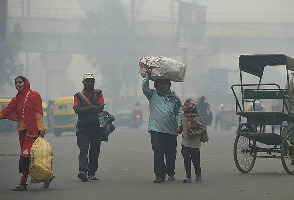 A family carries belongings while looking for a rickshaw amid heavy smog in New Delhi. — AFP
