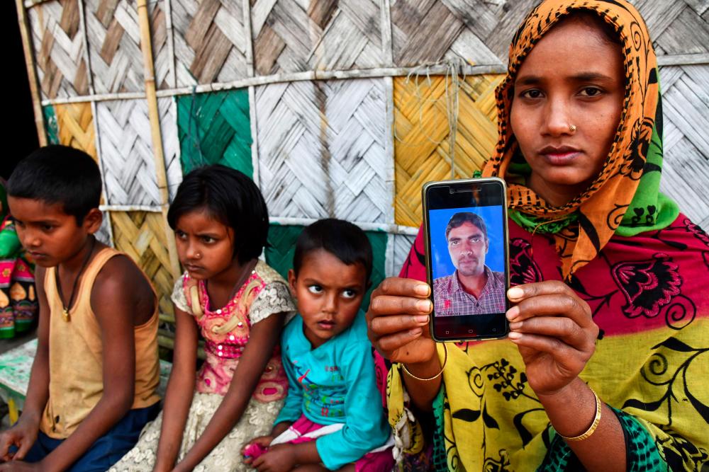 In this picture taken on Dec 30, 2018, Sajeda Khatun, wife of Saher Islam, who is still trapped after an illegal coal mine became flooded on Dec 13, shows her husband's photograph on her mobile phone as she sits with her children at her house in Bhangmari village in Chirang district of Assam. — AFP