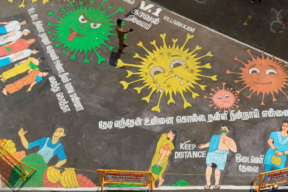 A policeman stands over a graffiti drawn to bring awareness on social distancing at a temporary market set up at a bus stand during a government-imposed nationwide lockdown as a preventive measure against the COVID-19 coronavirus, in Chennai on April 9, 2020. — AFP