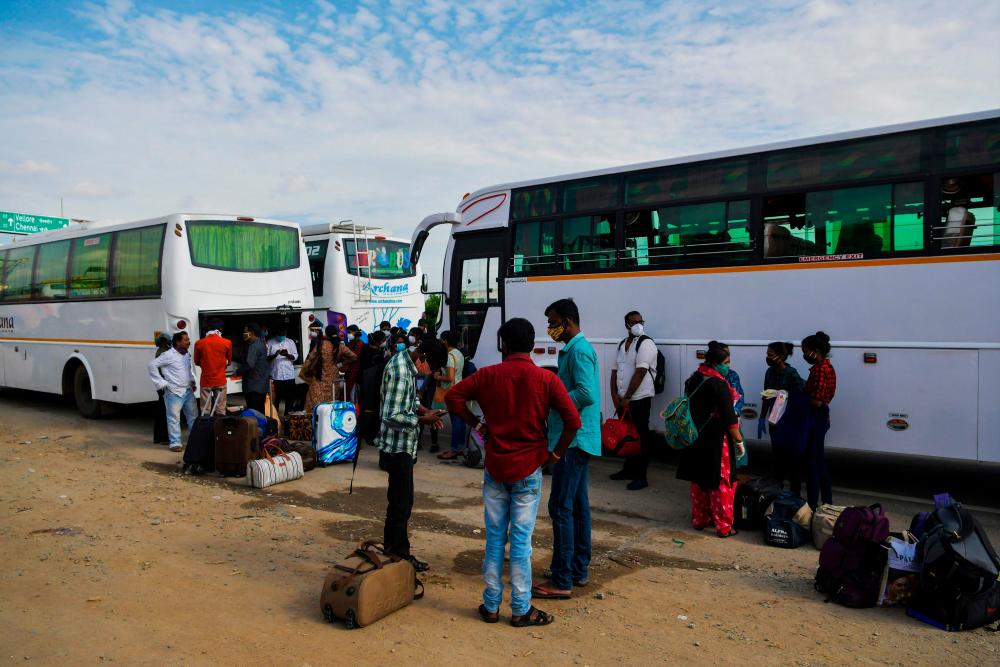 People wait to board buses and return to their home towns at the Karnataka-Tamil Nadu state border on the outskirts of Bangalore on July 13, 2020, as another lockdown is underway in Bangalore in an attempt to contain the surge of COVID-19 coronavirus cases. — AFP