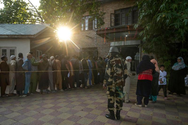 An Indian security personnel stands guard as voters queue up to cast their ballots at a polling station during the first phase of assembly elections in Pulwama, south of Srinagar on September 18, 2024. - AFPPIX