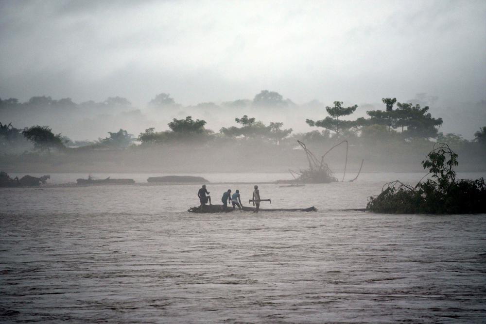 Indian men catch a tree in the flooded Manas river, following heavy rainfall in Baksa district of Assam, in the North-Eastern states of India. — AFP