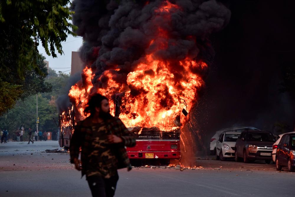 A man walks on a street as a bus is on fire following demonstration against the Indian government's Citizenship Amendment Bill (CAB) in New Delhi on Dec 15. — AFP