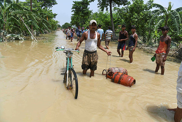An Indian resident wades on a flooded road leading his bicycle and carrying gas bottles following heavy monsoon rains at Muzaffarpur district in the Indian state of Bihar today. — AFP