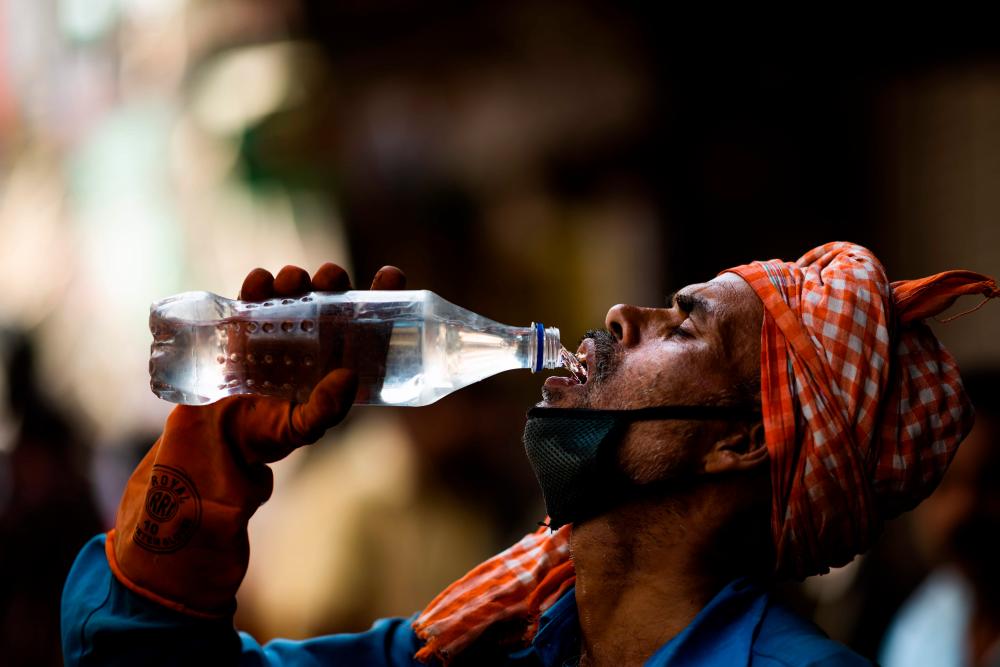 A labourer quenches his thirst with water from a bottle on a street amid rising temperatures in New Delhi on May 27, 2020. — AFP