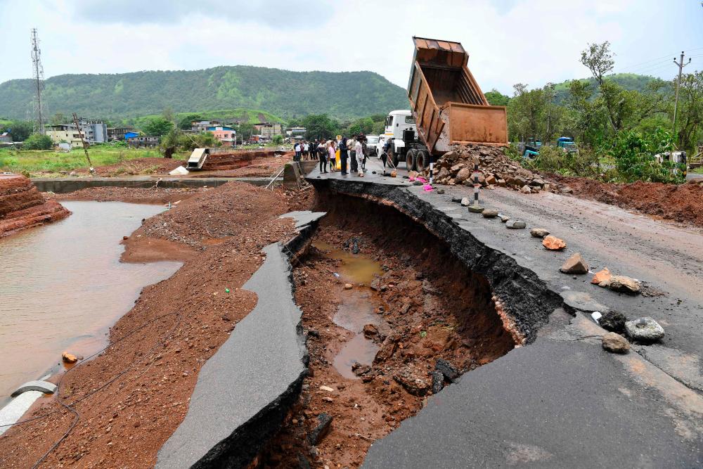 People gather along a road partially washed away at Mahad on July 24, 2021, as the death toll from heavy monsoon rains climbed to 79, with nearly 100,000 others evacuated in the western state of Maharashtra. -AFP