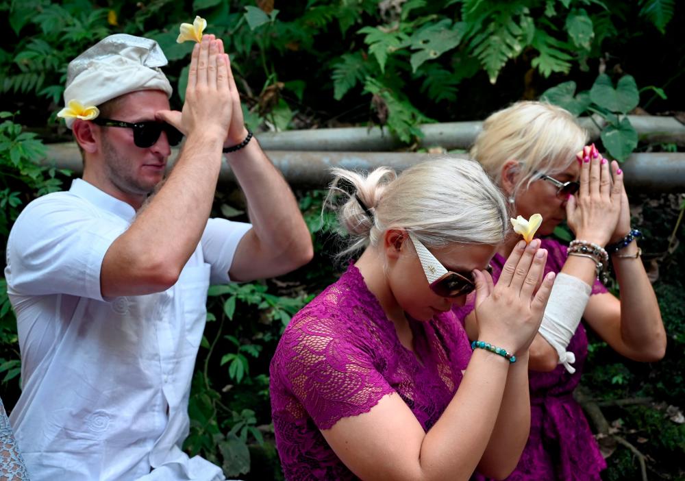 Czech nationals Sabina Dolezalova (centre R) and her boyfriend Zdenek Slouka (L) pray ahead of a purification ritual at the Beji Temple, located inside a monkey sanctuary in Ubud on Indonesia's resort island of Bali on Aug 15, after a disrespectful online video they posted went viral. — AFP