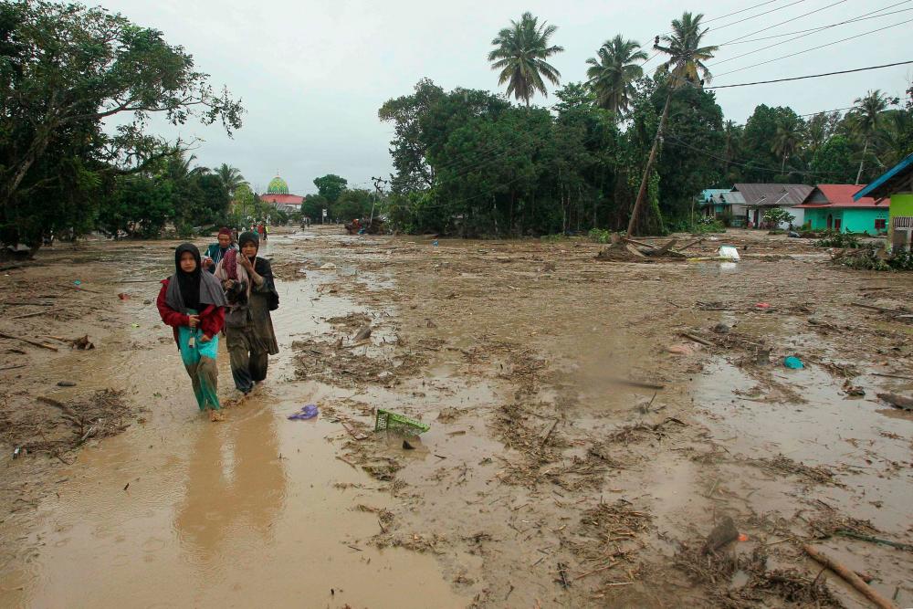 Villagers walk through a flooded area in Radda village in North Luwu regency, South Sulawesi on July 14, 2020, after three rivers overflowed due to torrential rains. At least 15 people died and dozens others were missing after flash floods caused by torrential rains left hundreds of houses buried in mud in Indonesia, authorities said. – AFP