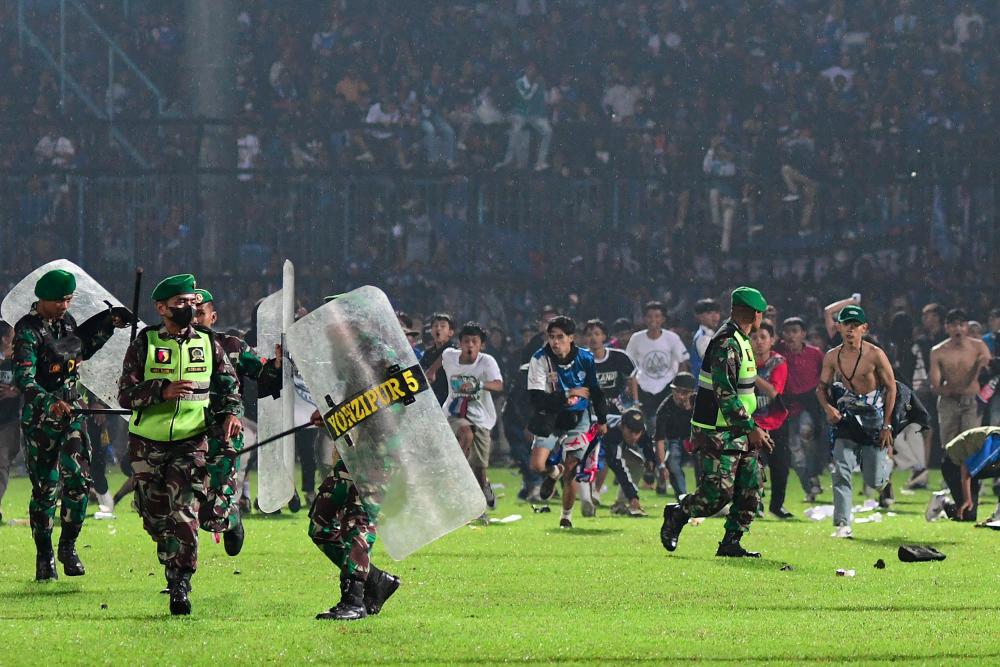 This picture taken on October 1, 2022 shows Arema FC supporters running on the pitch towards members of the Indonesian army after a football match between Arema FC and Persebaya at the Kanjuruhan stadium in Malang, East Java. - AFPPIX