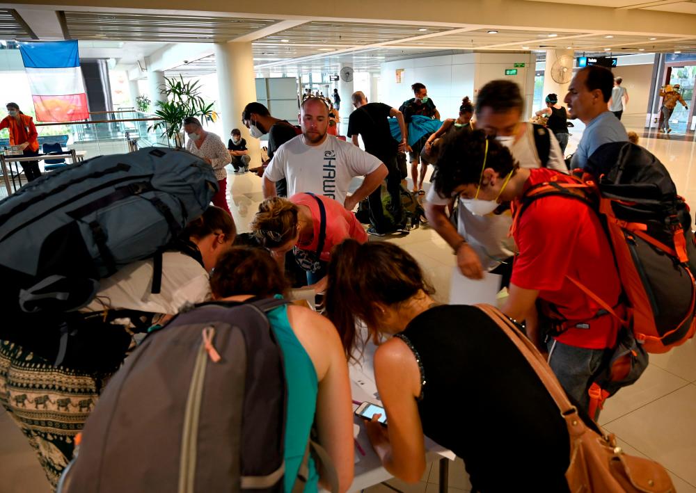 Stranded tourists fill forms ahead of their evacuation flight amid concerns from the COVID-19 coronavirus at the Ngurah Rai international airport near Denpasar, Indonesia's resort island of Bali, on March 28, 2020. — AFP