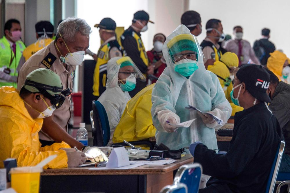 Indonesian officials conduct health screening on 156 migrant workers who arrived from Malaysia at Surabaya airport in Indonesia's East Java on April 7, 2020, amid concerns of the spread of the Covid-19 coronavirus. — AFP
