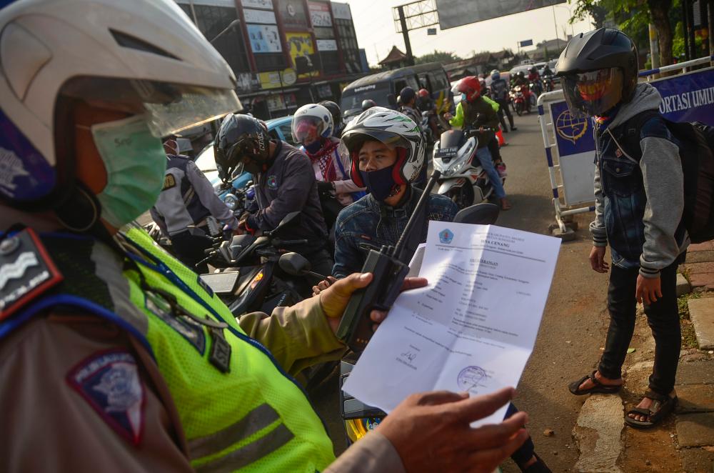 An Indonesian police officer inspects a document from a motorist heading toward the capital city of Jakarta, in Bekasi, West Java, on May 29, 2020, amid travel restrictions during the Covid-19 coronavirus pandemic. - AFP
