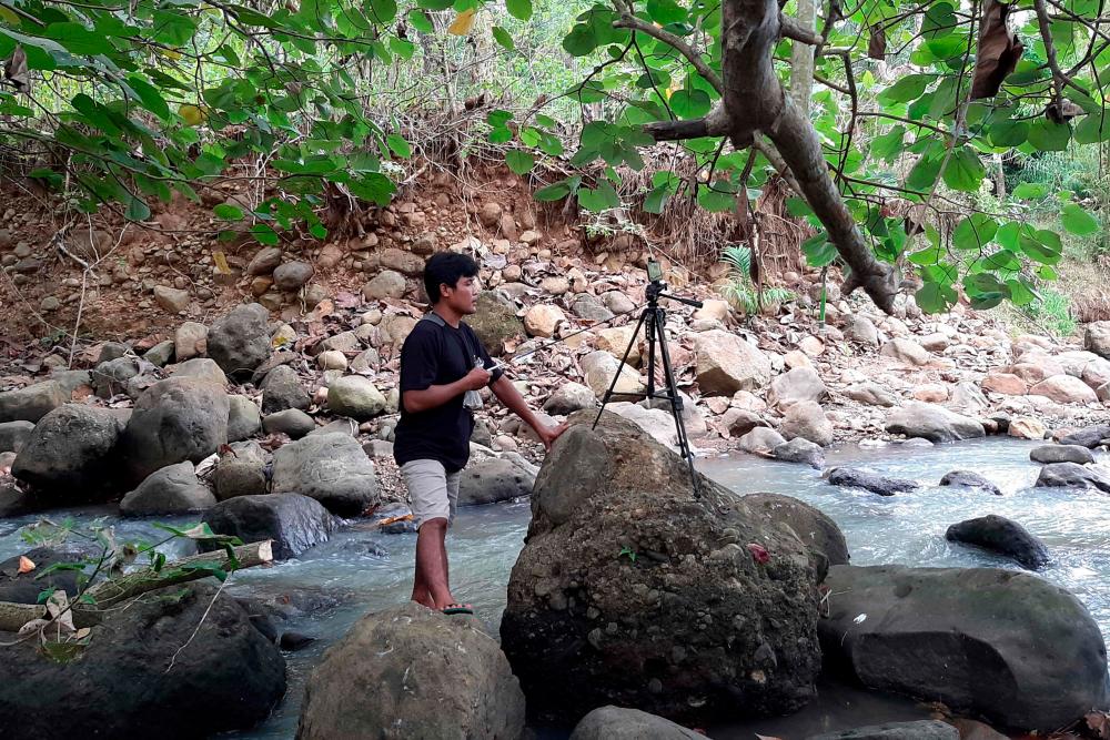 This picture taken on June 16, 2021 shows Indonesian YouTuber Siswanto recording one of his videos next to a water stream in a farming community in Banyuwangi. -AFP