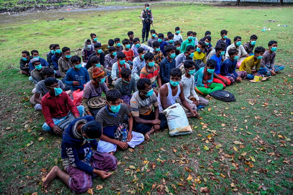 A policeman (top) stands guard next to a group of Rohingya refugees waiting to be transferred to a temporary shelter following their arrival by boat in Krueng Raya, Indonesia’s Aceh province on December 25, 2022/AFPPix