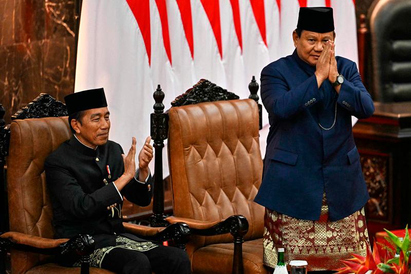 Indonesia's new President Prabowo Subianto (R) gestures as his predecessor Joko Widodo (L) applauds during the presidential inauguration at the Parliament building in Jakarta on October 20, 2024. Former general Prabowo Subianto was sworn in October 20 as president of Indonesia, seeking a more prominent position on the global stage for the world's fourth most populous nation. - BAY ISMOYO / AFP