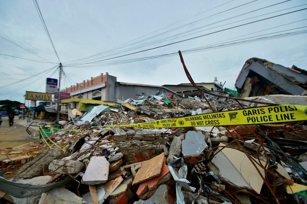 People walk by collapsed shops in Mamuju on January 17, 2021, after a 6.2-magnitude earthquake rocked Indonesia’s Sulawesi island. / AFP / Firdaus
