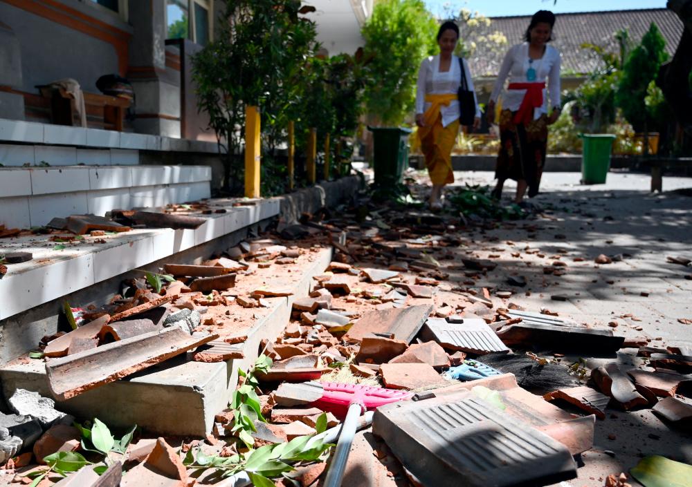 Two teachers walk past tiles which fell off the damaged roof of a school building after a earthquake hit the area in Jimbaran on Indonesia’s resort island of Bali on July 16, 2019. — AFP