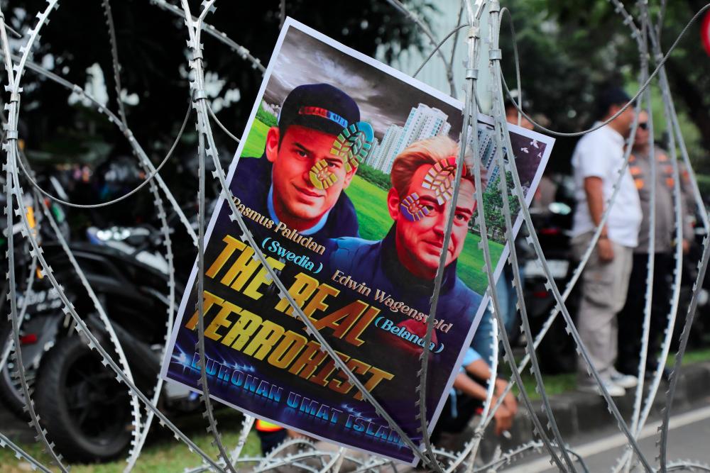 A placard against Swedish-Danish far-right politician Rasmus Paludan (L) Edwin Wagensveld (R), a Dutch far-right leader of an anti-Islam group, is seen on razor wire fencing as demonstrators gather outside the Swedish Embassy in Jakarta on January 30, 2023 - AFPPIX