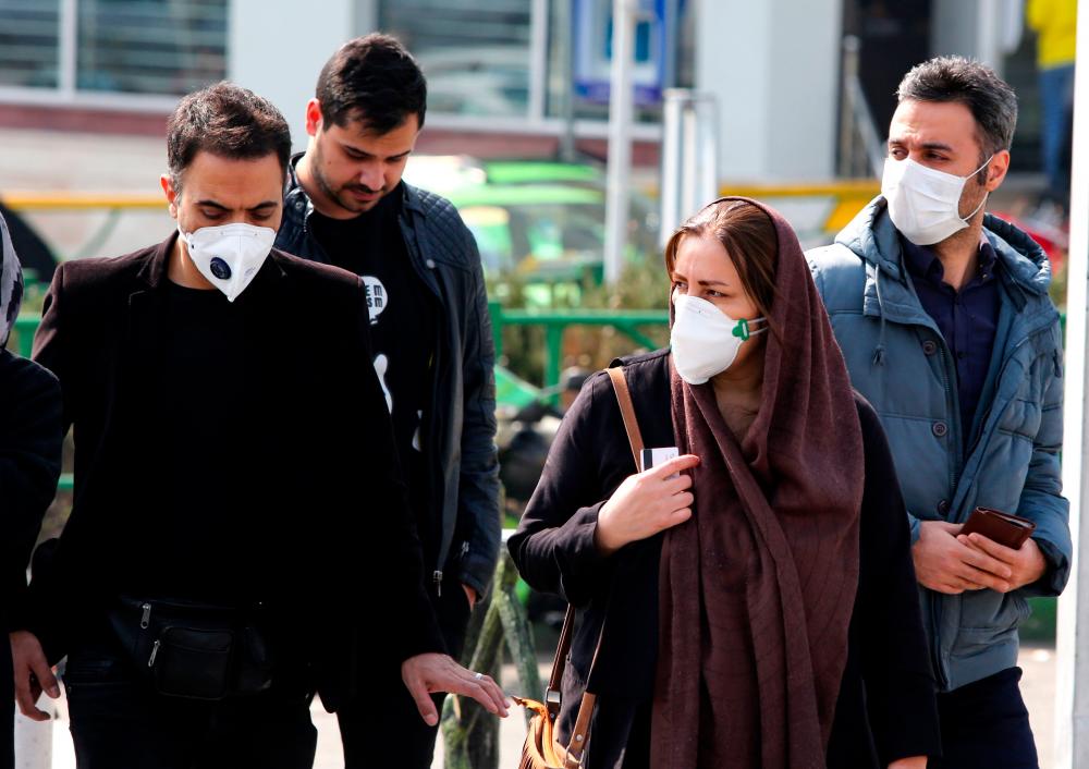 Iranians, some wearing protective masks, wait to cross a street in the capital Tehran on February 22, 2020. - AFP