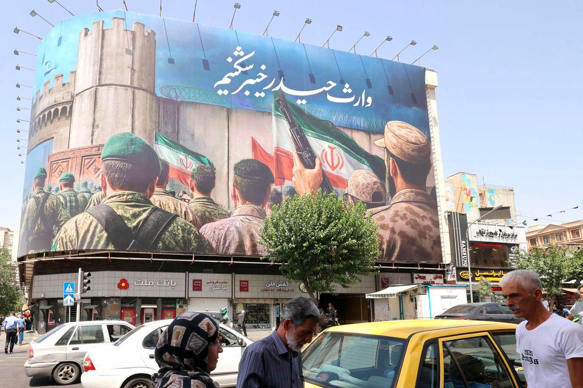 People walk past a huge banner on Enghelab (Revolution) Square, in Tehran on June 24, 2025. (Photo by ATTA KENARE / AFP)
