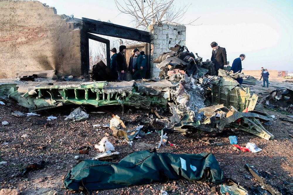 People stand near the wreckage after a Ukrainian plane carrying 176 passengers crashed near Imam Khomeini airport in Tehran on Jan 8. — AFP