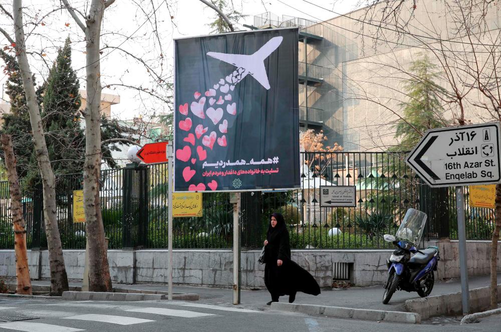 An Iranian woman walks beneath a poster honouring the victims of a Ukrainian passenger jet accidentally shot down in the capital last week, in front of the Amirkabir University in the capital Tehran, on Jan 13. — AFP