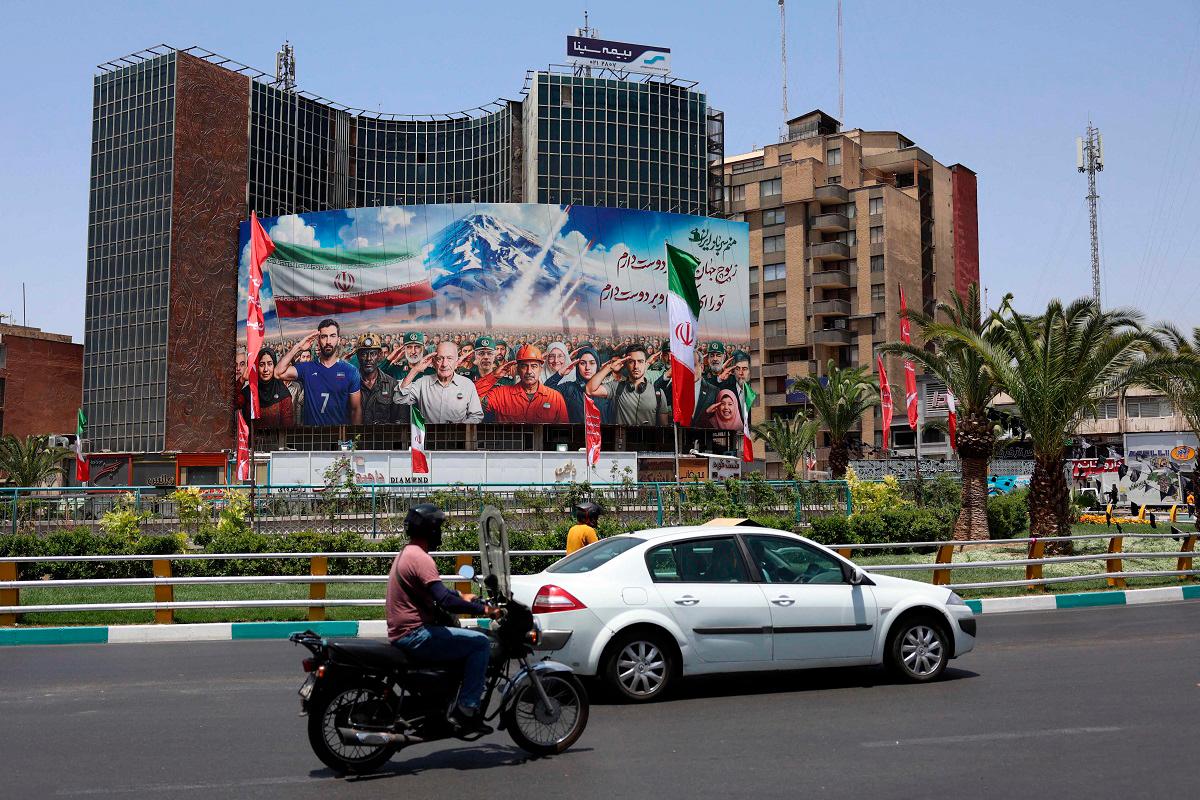 A banner bearing a painting that represents various categories of the Iranian society is deployed against the facade of a building in Tehran, with a message that reads in Farsi: “ we are all soldiers of Iran”, on June 22, 2025. - AFPpix